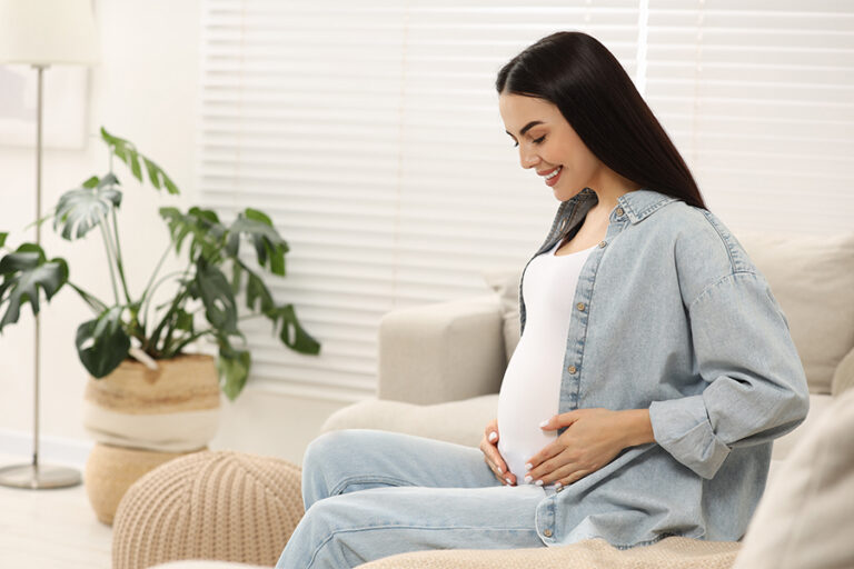 Happy pregnant woman on sofa at home, space for text